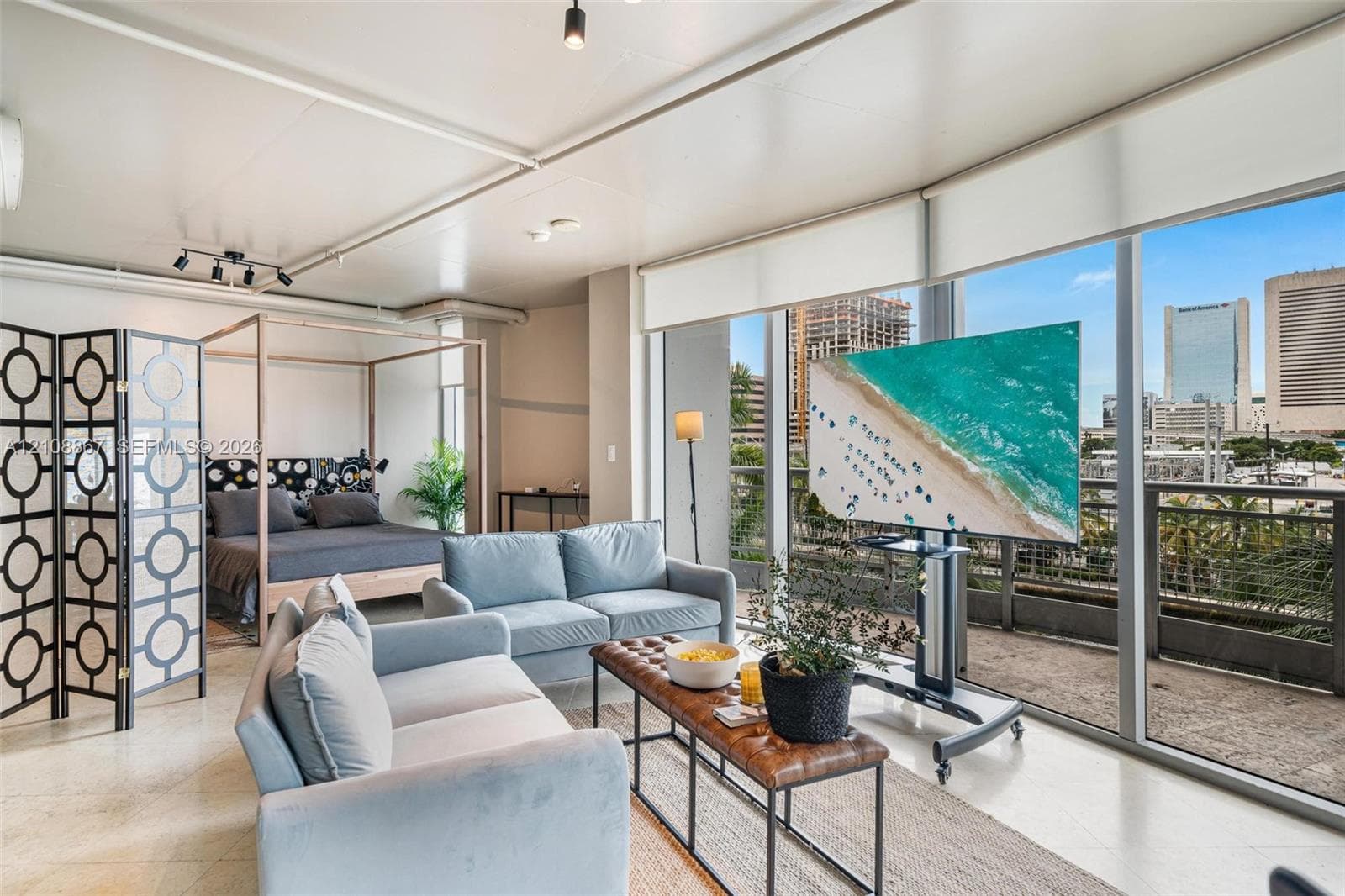 Floor-to-ceiling windows, light-toned stone-finish flooring, industrial-style track lighting, and a private balcony with metal railing
