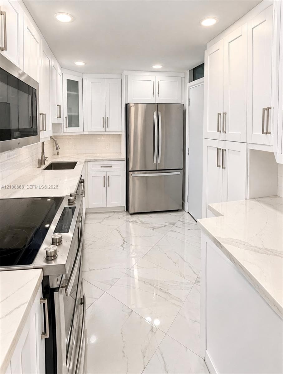 Kitchen featuring white shaker-style cabinetry, solid-surface countertops with a subway tile backsplash, stainless steel appliances, and large-format tile flooring