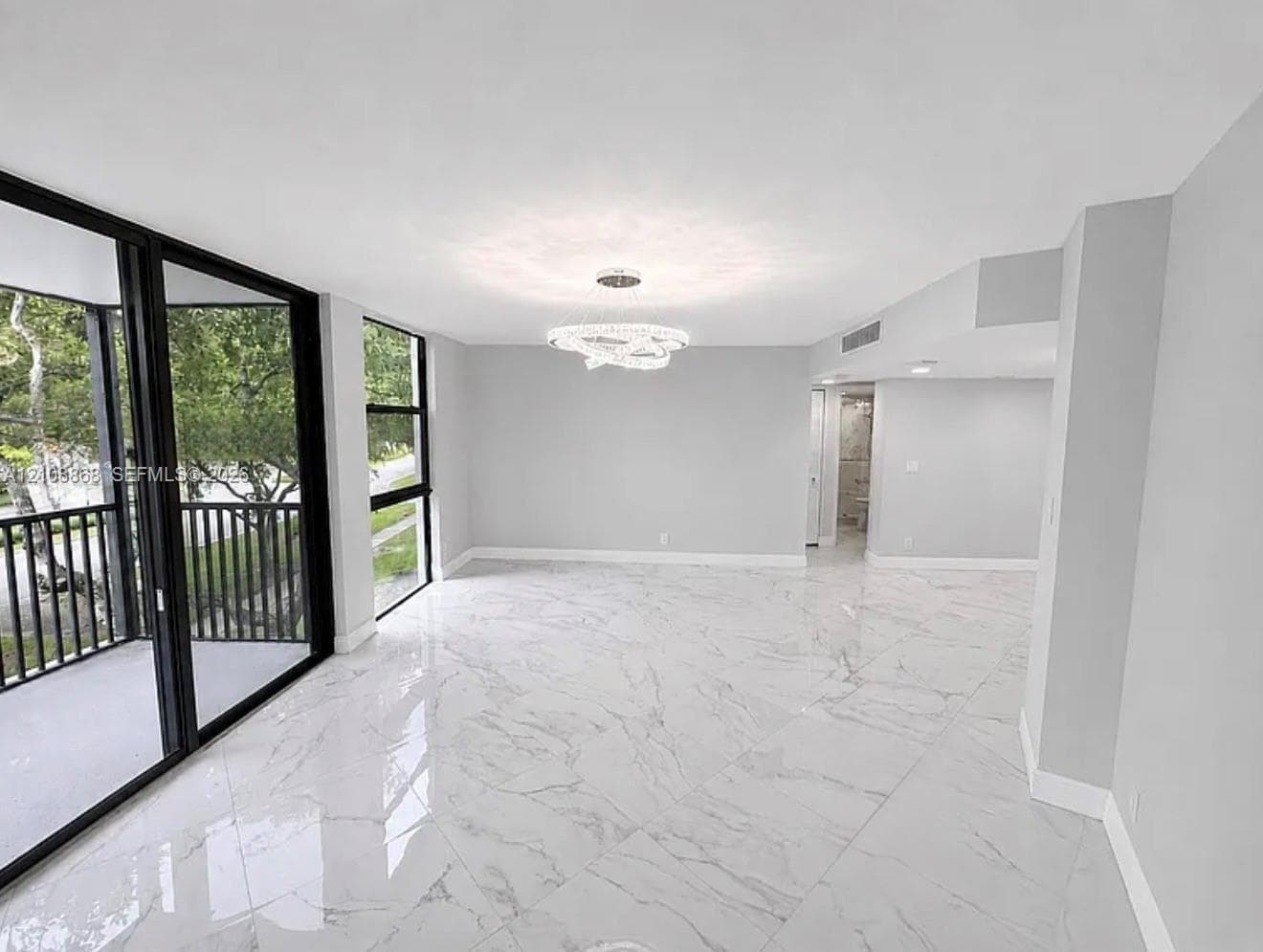 Large-format tile flooring with polished finish, expansive sliding glass doors, black-framed balcony railing, and modern multi-tiered LED chandelier