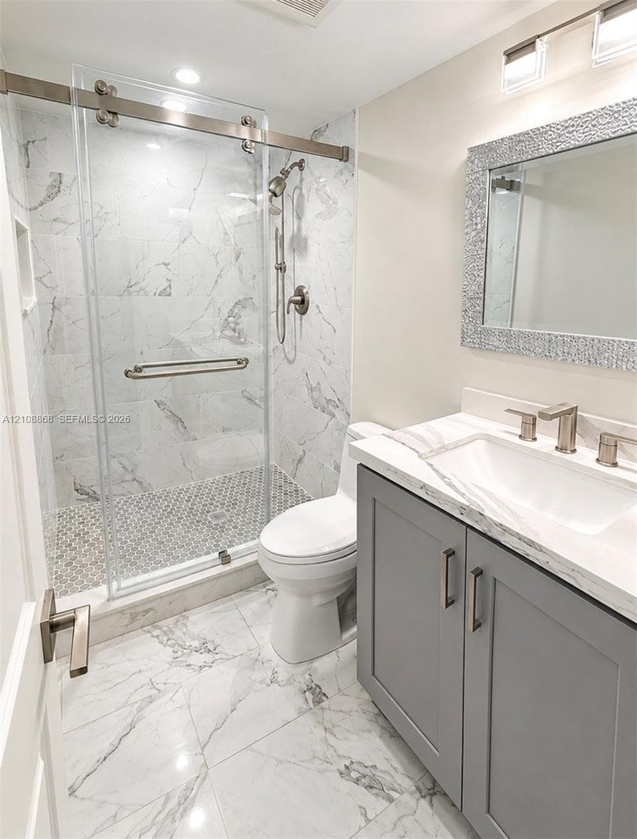 2nd bath Bathroom featuring a walk-in shower with sliding glass door, stone-patterned tile flooring, gray shaker-style vanity with stone-composite countertop, and wall-mounted vanity lighting