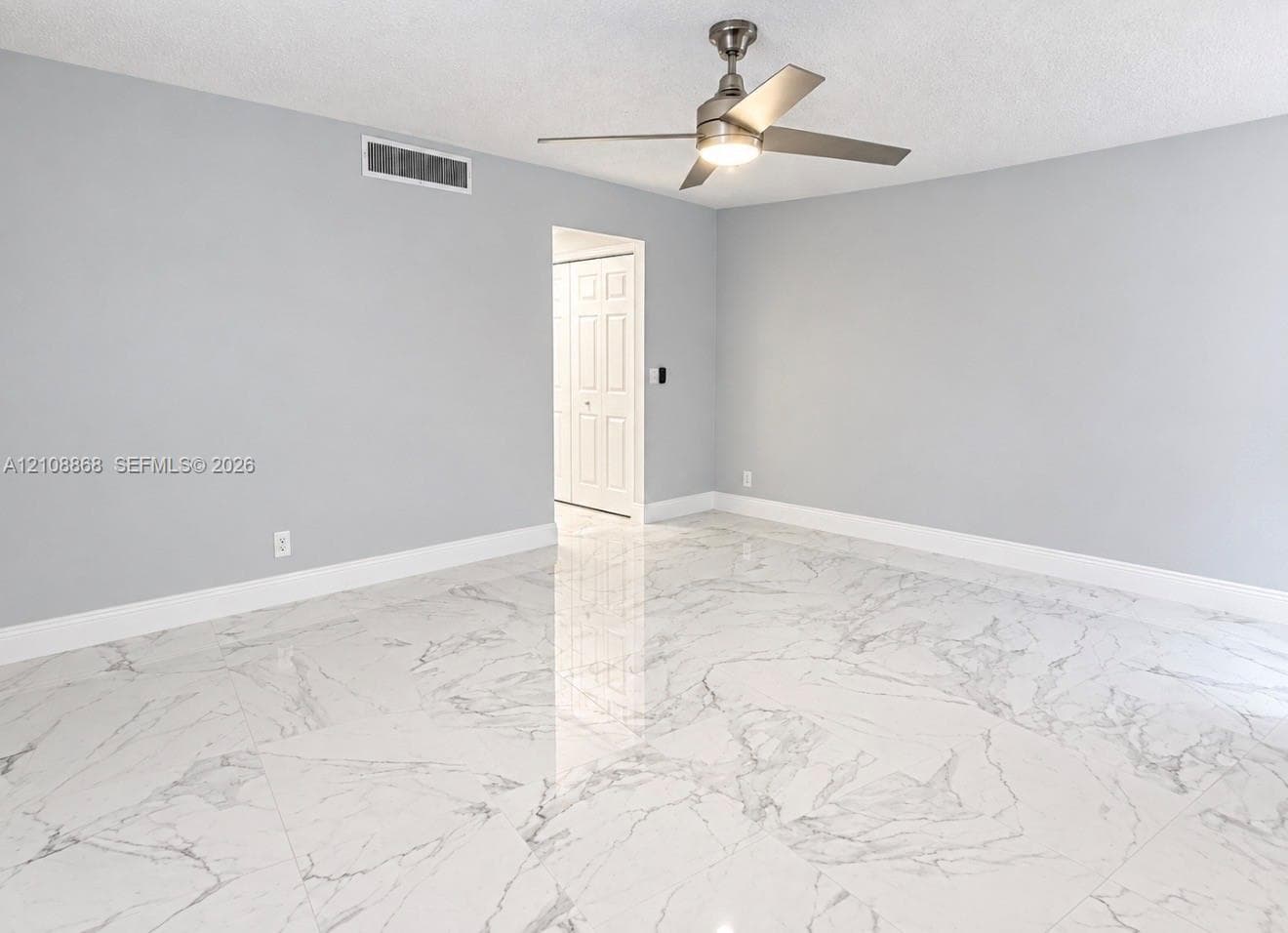 Master bedroom. Large-format polished tile flooring featuring a vein-patterned finish, metallic ceiling fan with integrated lighting, and multi-panel bi-fold closet doors