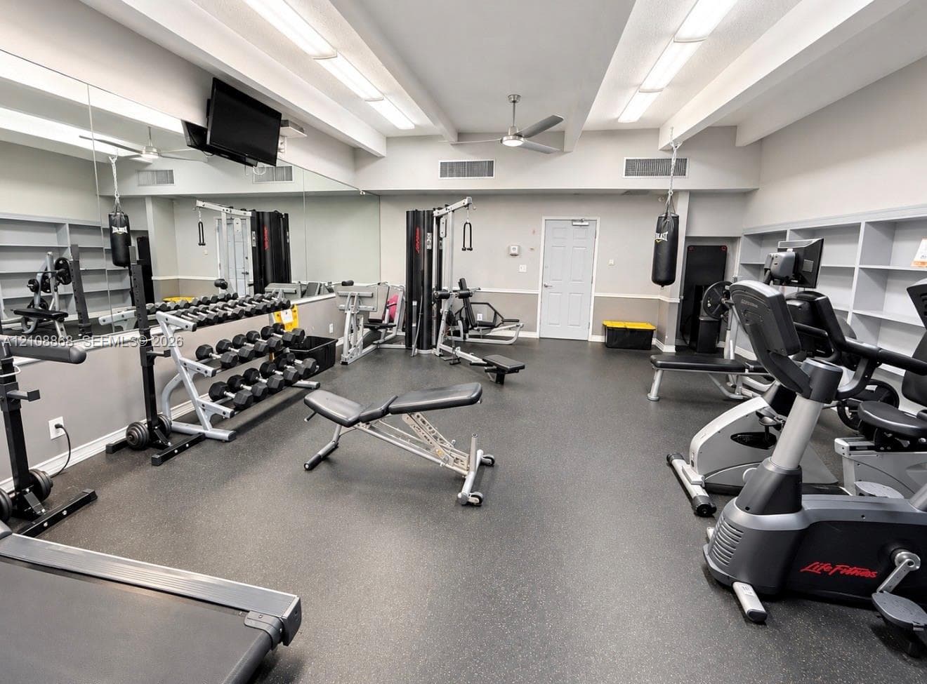 Fitness space featuring expansive wall-to-wall mirror, built-in shelving, rubberized flooring, and recessed ceiling lighting