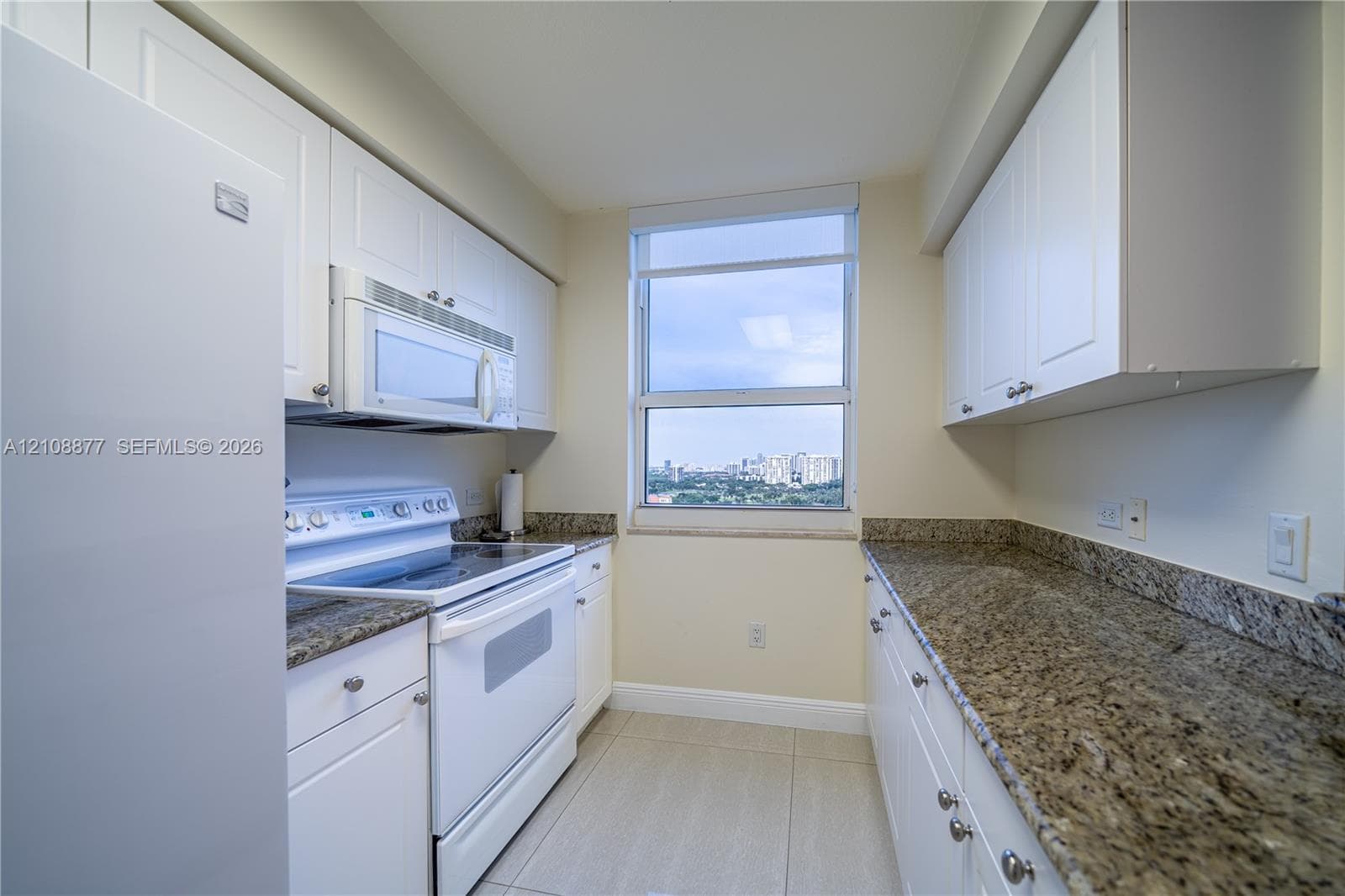 Kitchen featuring white cabinetry, stone countertops, integrated white appliances, and large-format tile flooring with an exterior urban backdrop