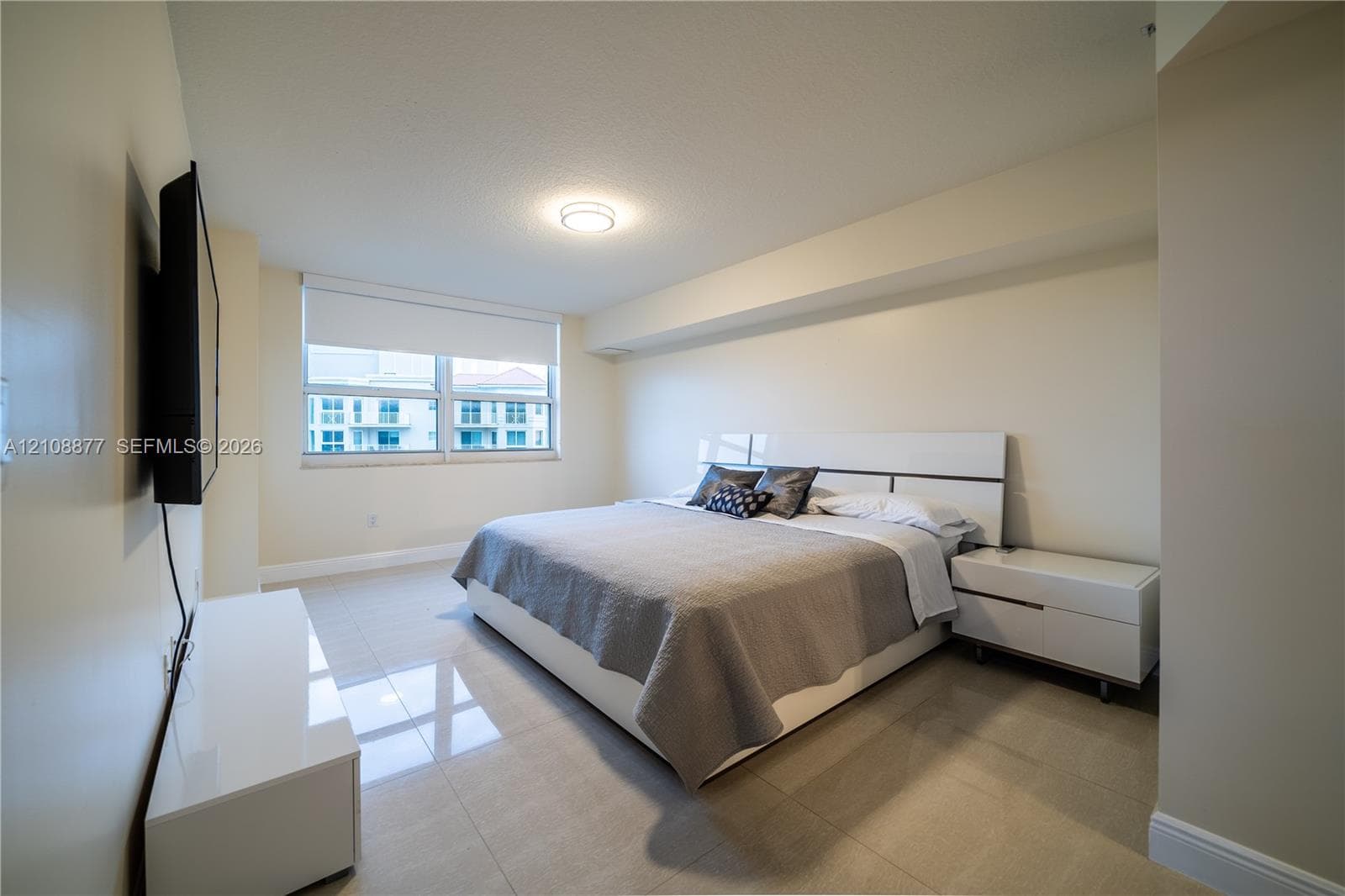 Neutral-toned room featuring large-format tile flooring, recessed ceiling lighting, and a window fitted with a roller shade