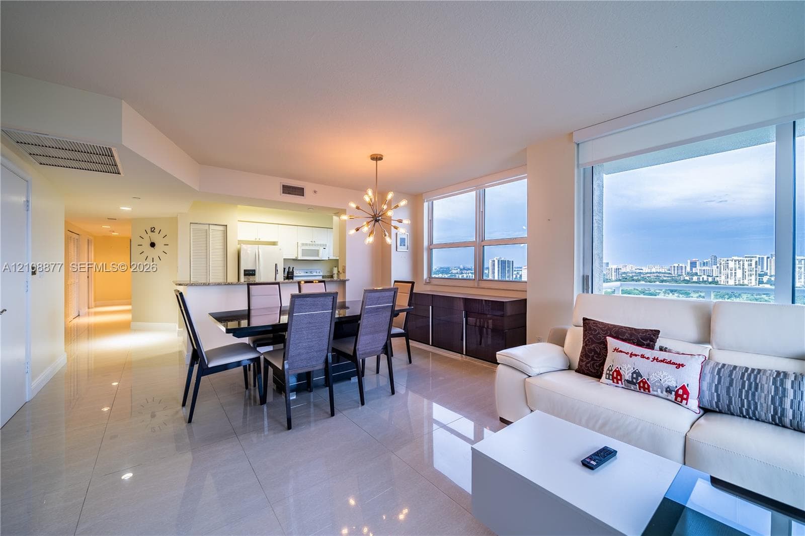 Open-concept living space featuring high-gloss tile flooring, floor-to-ceiling windows, built-in kitchen cabinetry with stone countertops, and a modern sputnik-style pendant light fixture