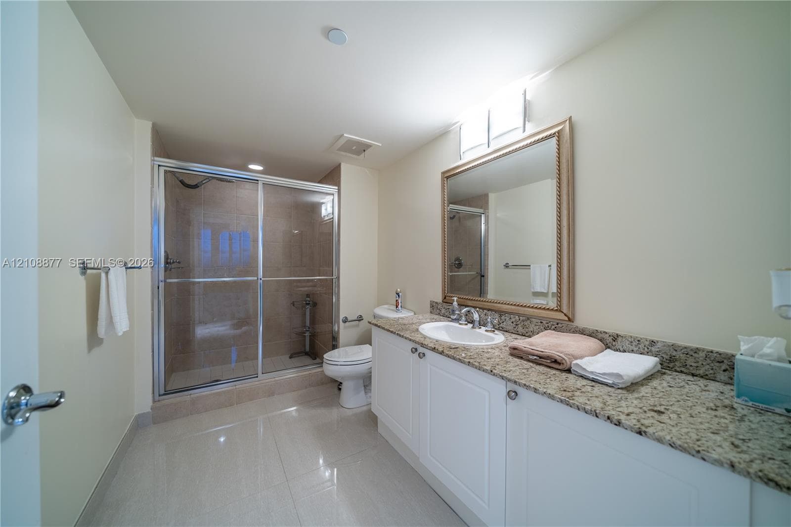 Bathroom featuring a white vanity with a stone countertop, an integrated sink, a framed mirror, and a glass-enclosed shower with tiled walls