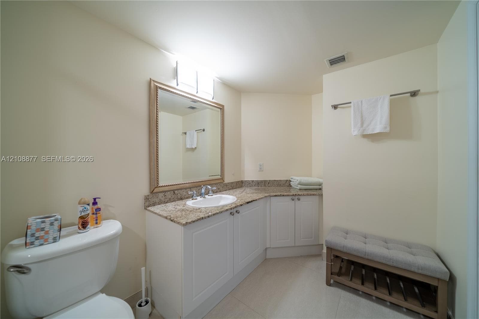 Bathroom featuring an L-shaped vanity with stone-surfaced countertop, integrated oval sink, under-cabinet storage, and framed wall mirror with integrated lighting