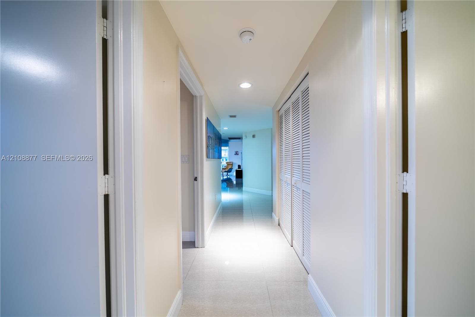 Hallway featuring light-toned tile flooring, recessed ceiling lighting, and built-in closet cabinetry with white louvered doors