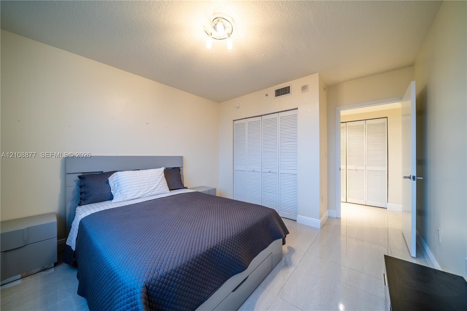 Bright room featuring large-format tile flooring, dual sets of bi-fold closet doors, and a ceiling-mounted light fixture