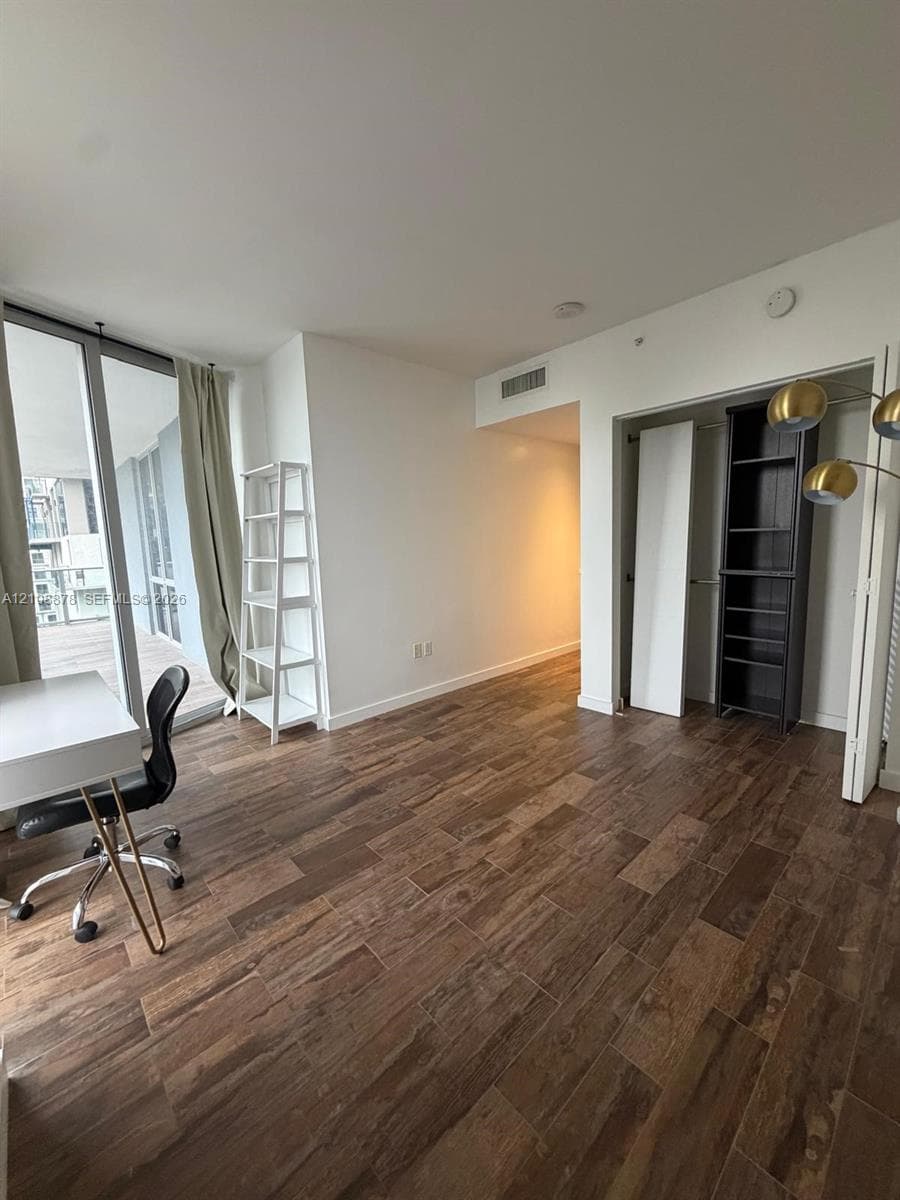 Floor-to-ceiling windows, wood-finish tile flooring, and a sliding glass door opening to a private balcony with metal railings