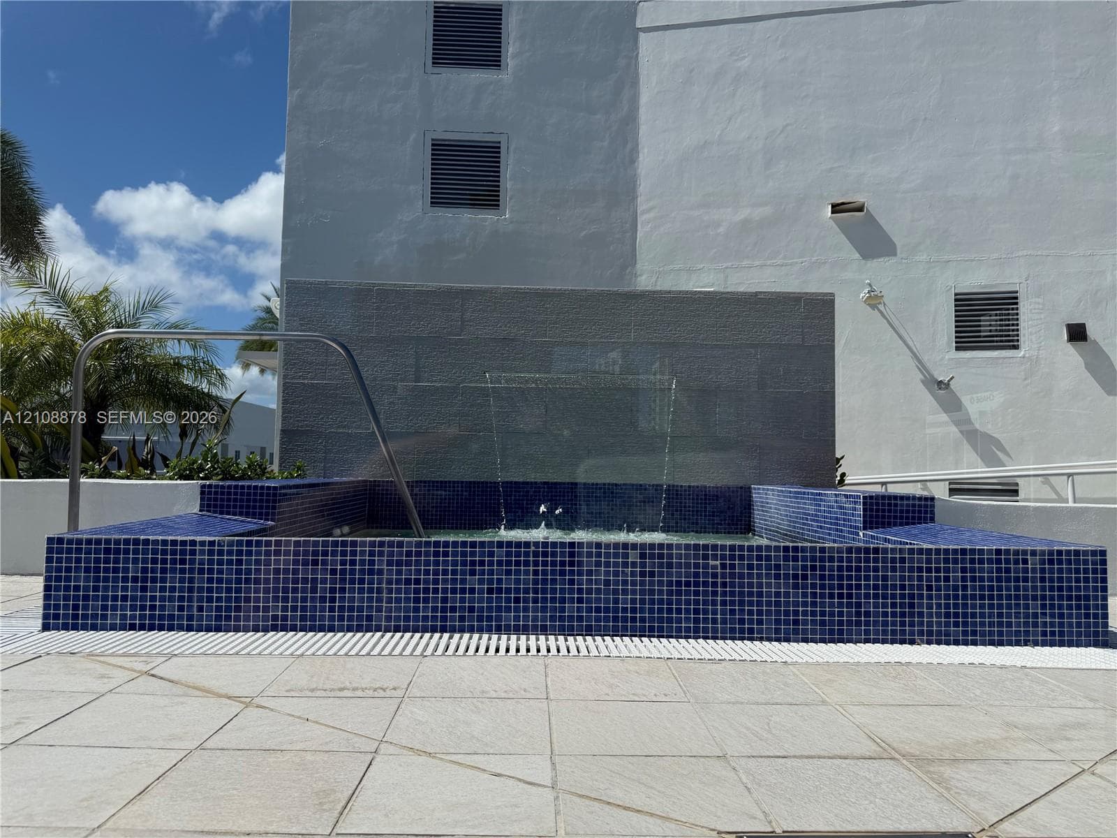 Rooftop terrace featuring light stone tile flooring, structural white overhead framing, glass-paneled railings, integrated planter boxes, and synthetic turf sections