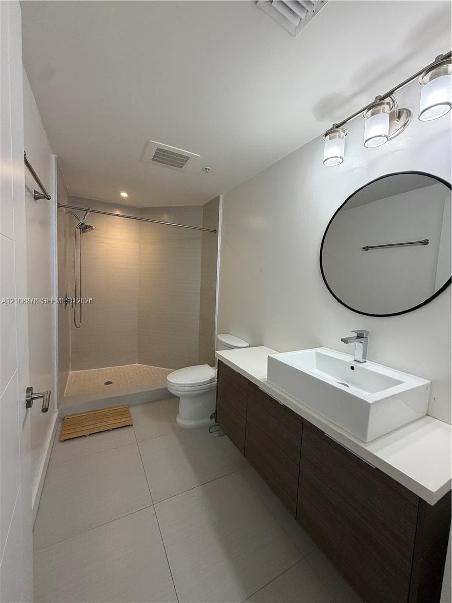 Floating vanity with rectangular vessel sink, white solid-surface countertop, walk-in shower with tiled surround, and circular wall-mounted mirror