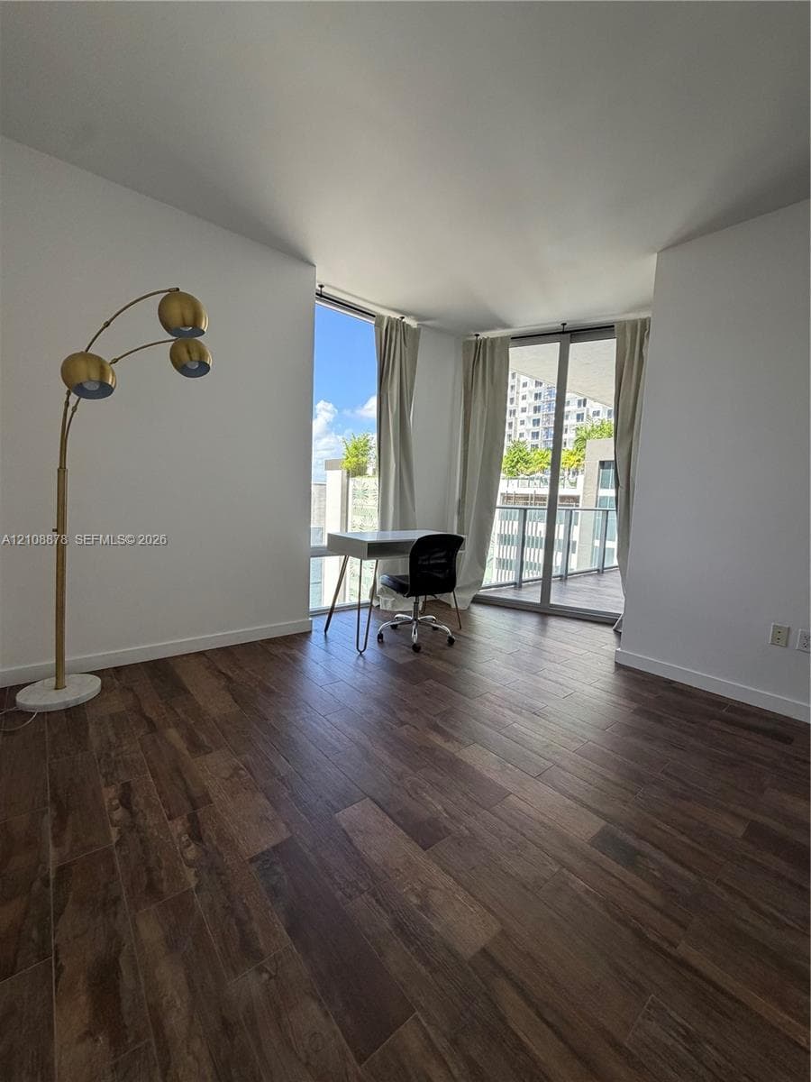 Room featuring wood-finish flooring, floor-to-ceiling windows, and balcony access with a metal railing