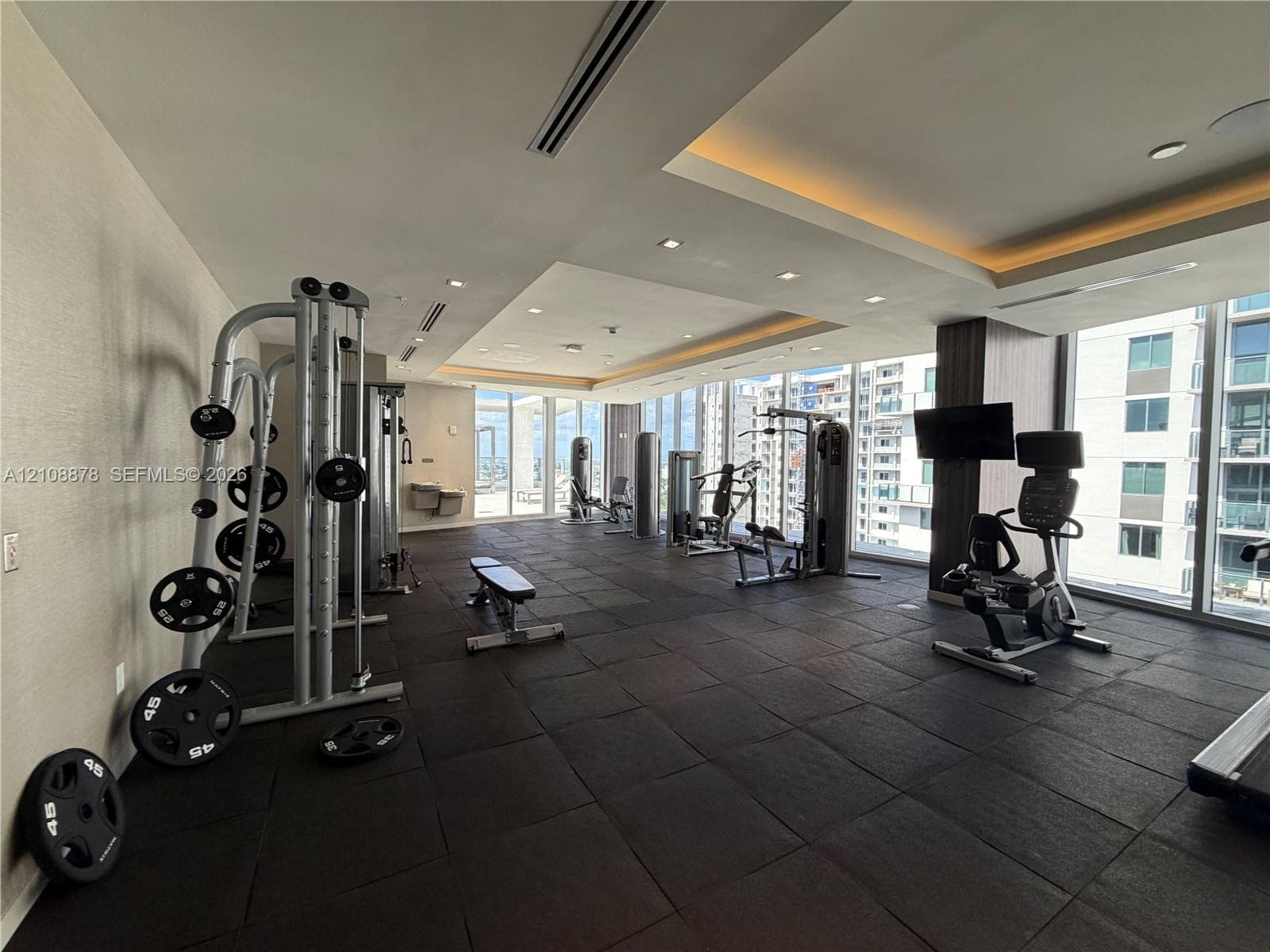 Fitness center featuring rubberized flooring, recessed tray ceiling lighting, floor-to-ceiling windows, and integrated ceiling speakers