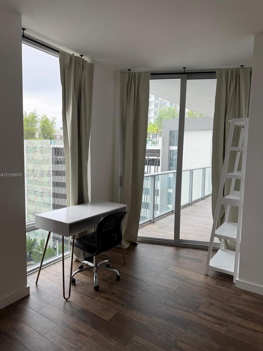 Floor-to-ceiling windows and sliding glass doors, wood-finish flooring, and a private balcony with glass railing