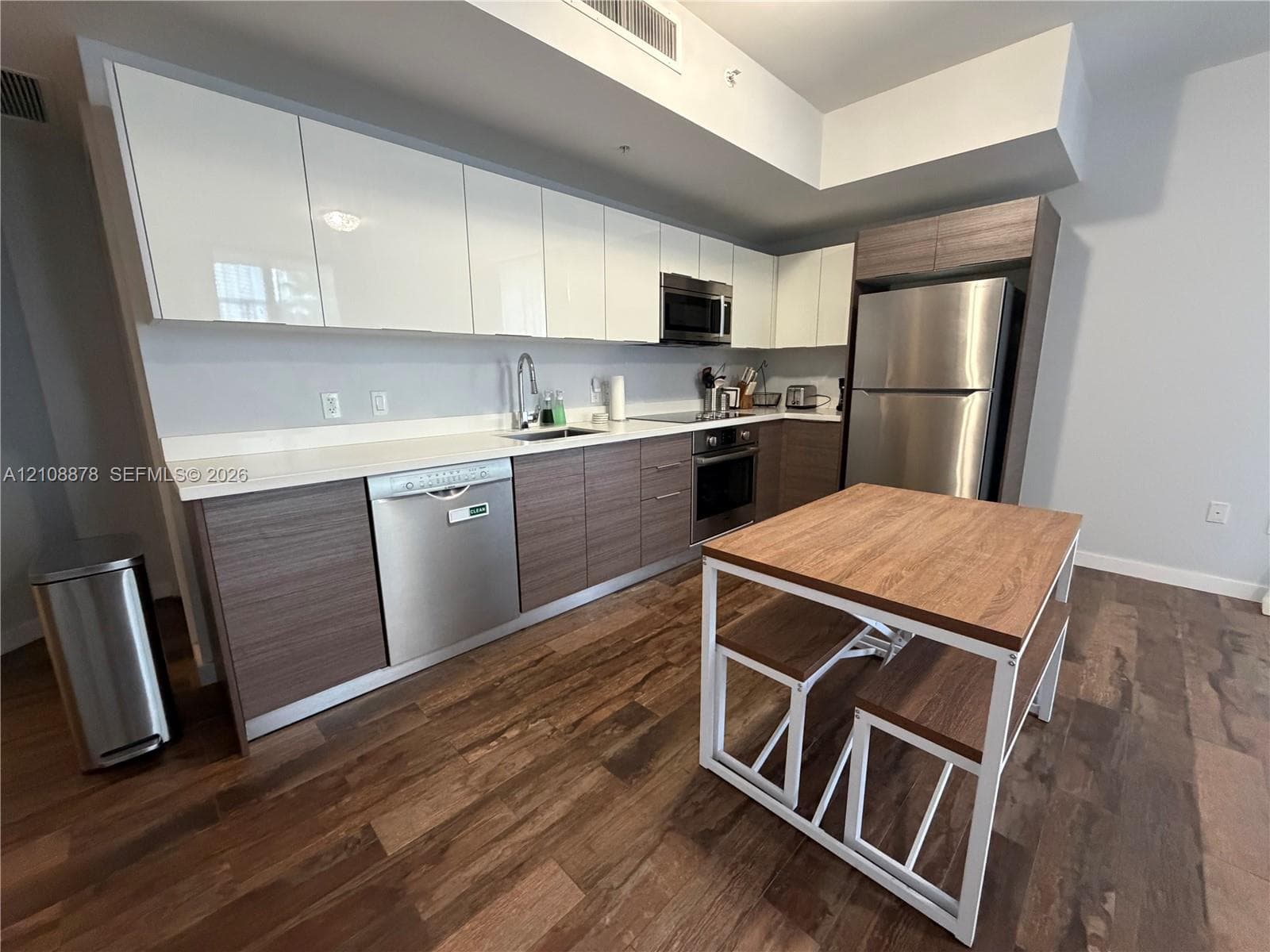 Open-concept interior featuring wood-finish flooring, stainless steel refrigerator, and recessed ceiling lighting