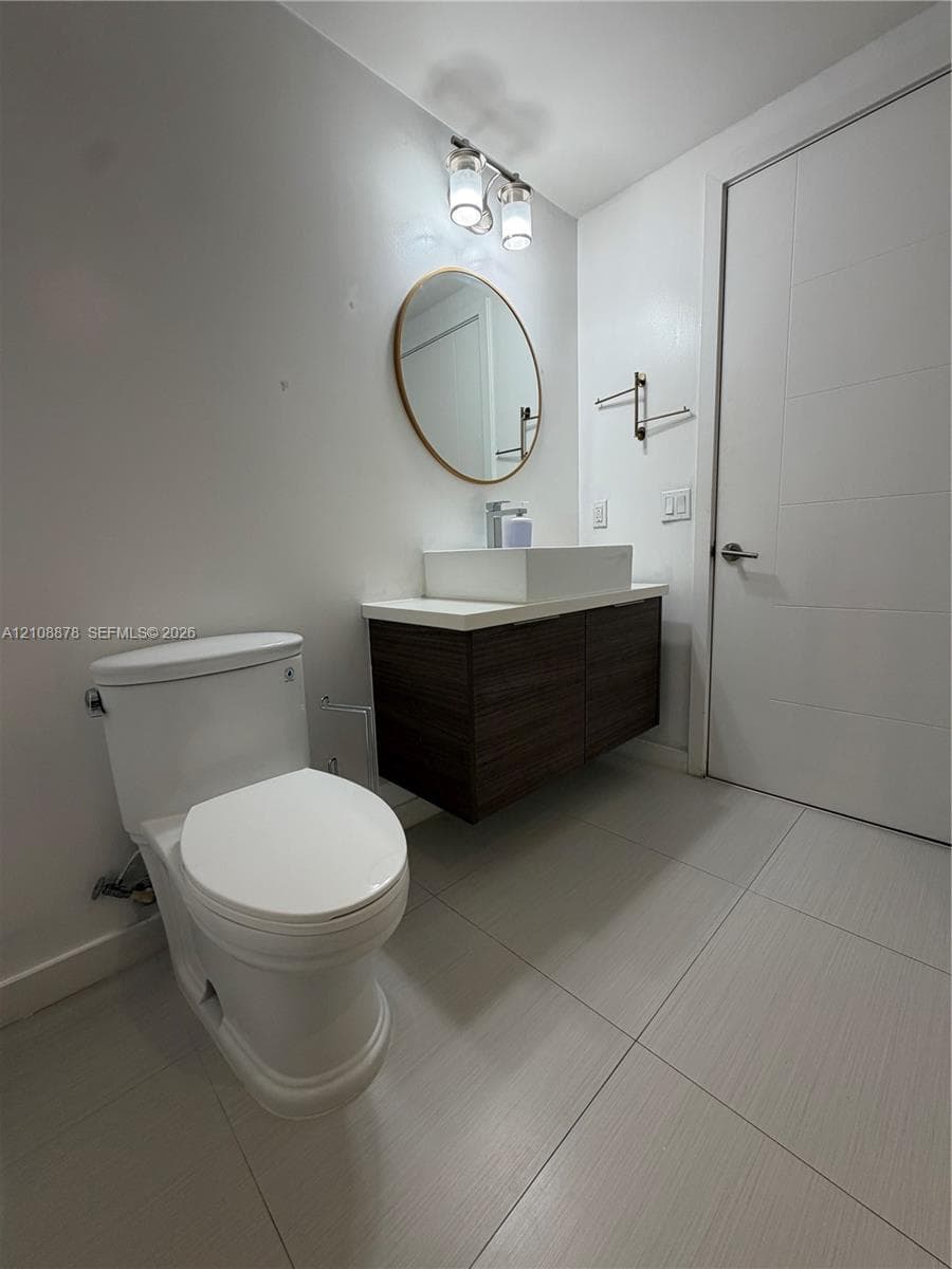 Bathroom featuring a built-in bathtub with a handheld showerhead, textured tile surround, large-format floor tile, and a floor-to-ceiling white bifold closet door