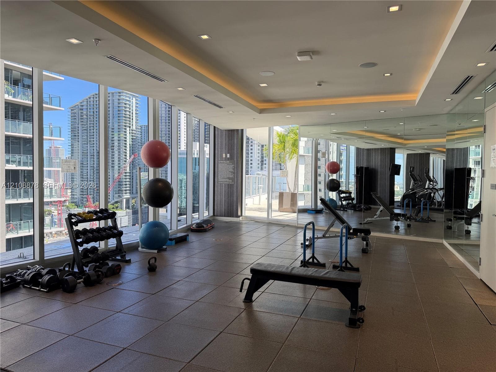 Fitness facility featuring floor-to-ceiling windows, tray ceilings with recessed lighting, and rubberized tile flooring