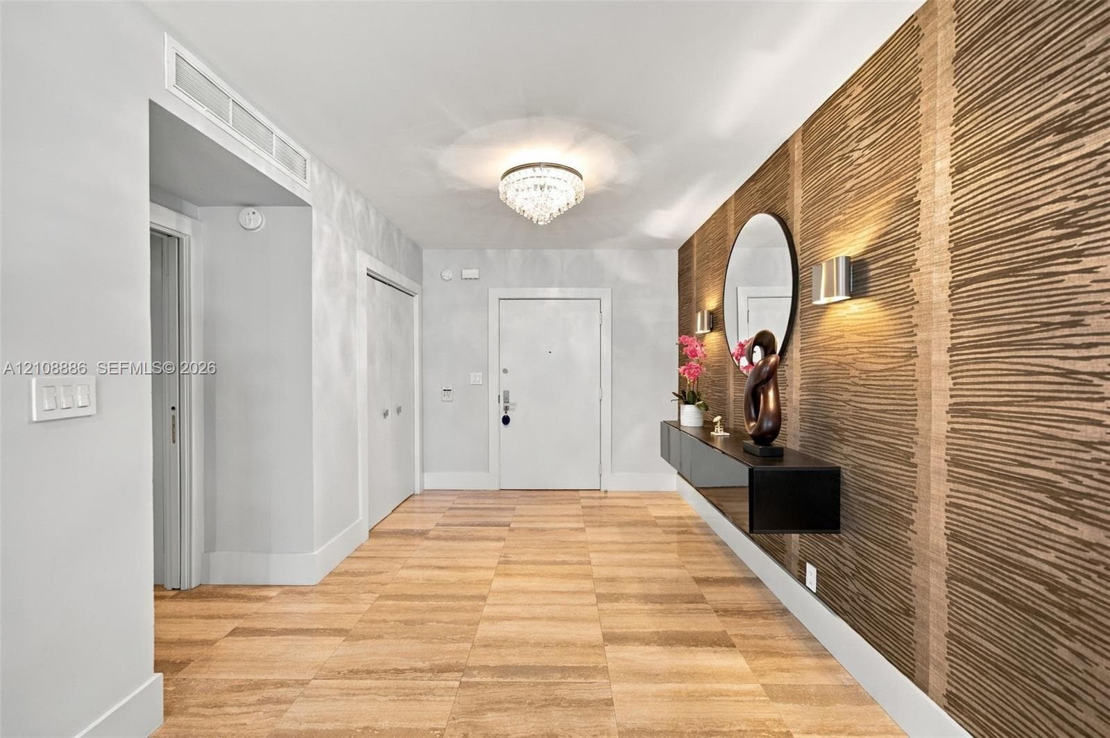 Entryway featuring wood-finish tile flooring, a statement wall with textured wall covering, a mounted floating console, and a tiered crystal flush-mount light fixture