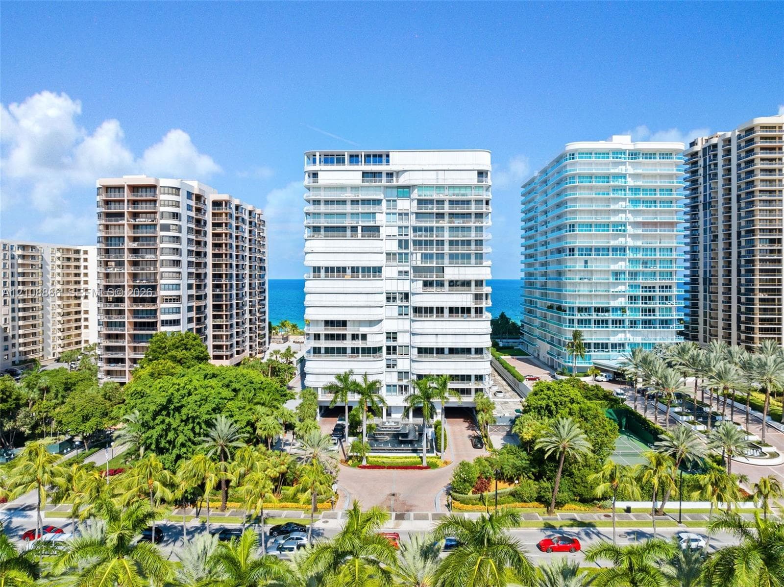 High-rise residential exterior featuring expansive glass balconies, a multi-story modern facade, mature palm tree landscaping, and direct access to the coastal shoreline