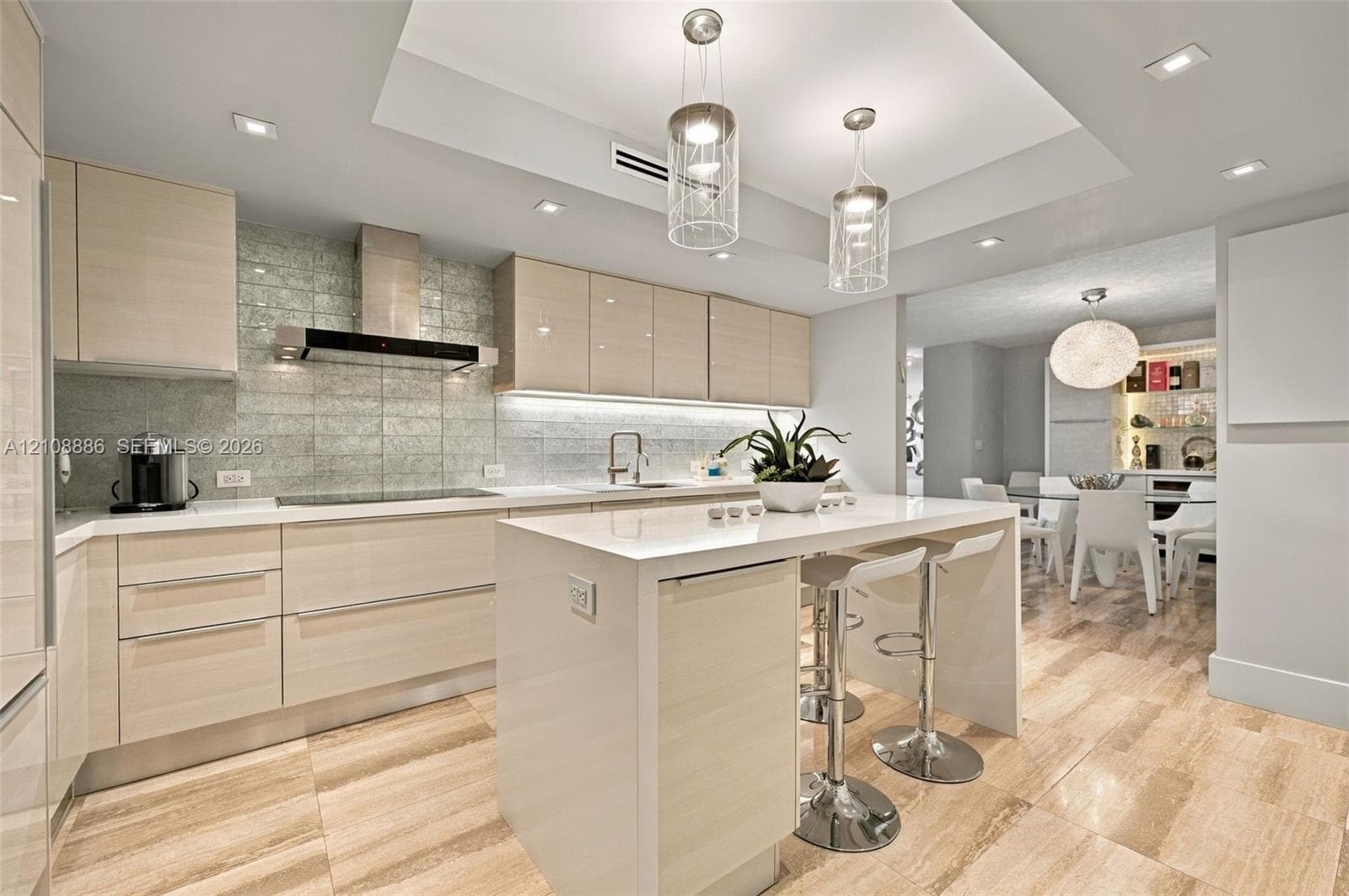 Kitchen featuring light wood-finish cabinetry, stone flooring, a center island with quartz-style waterfall countertop, glass tile backsplash, and stainless steel range hood