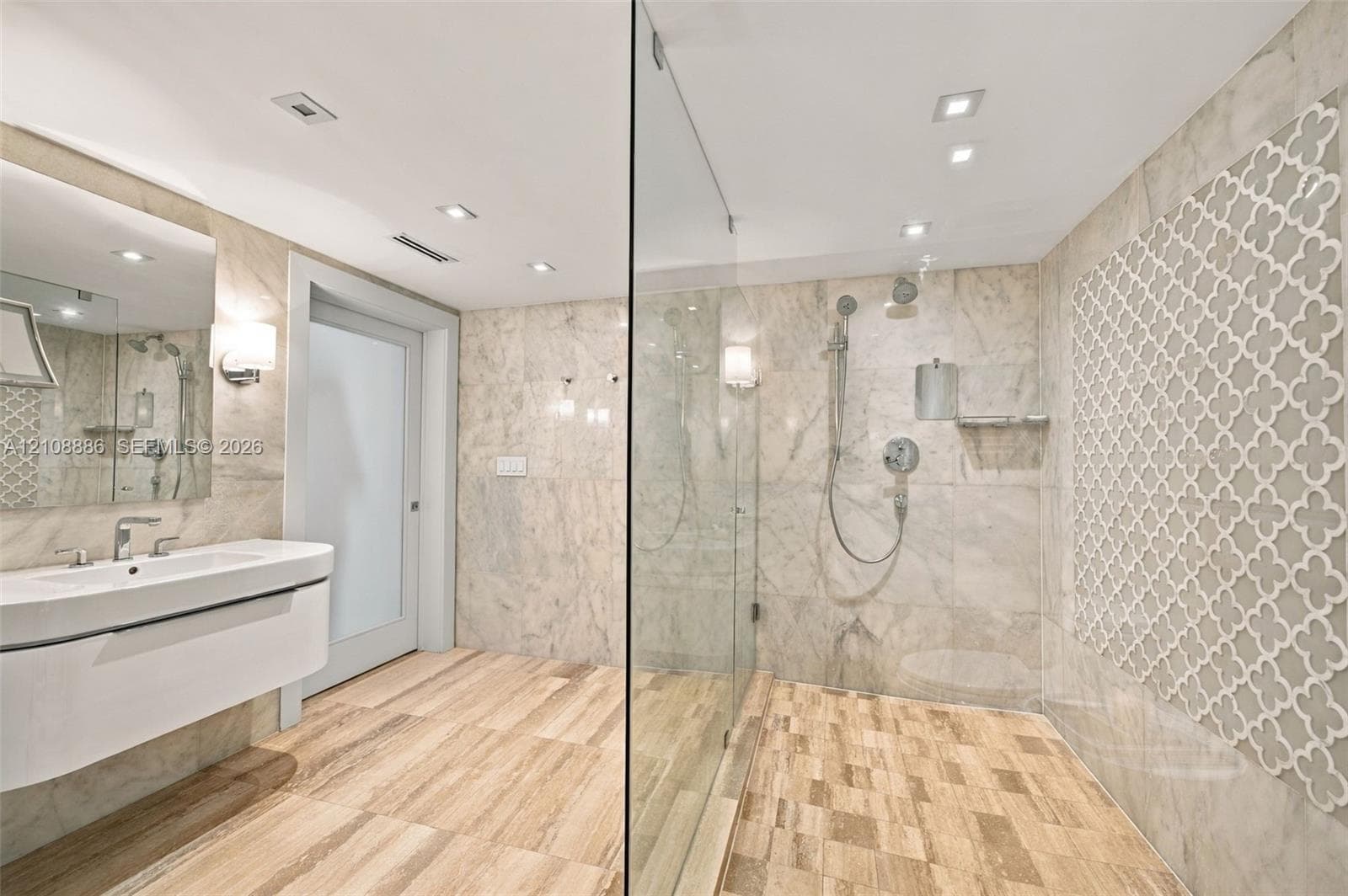 Floating vanity with integrated sink, walk-in glass-enclosed shower, stone wall tiling, decorative geometric tile accent wall, and recessed ceiling lighting