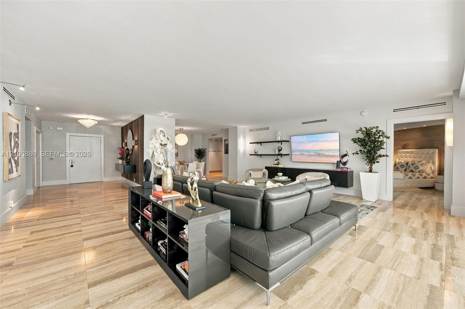 Open-concept interior featuring expansive stone-tile flooring, custom dark wood-finish accent wall, built-in recessed lighting, floating wall-mounted shelving, and minimalist-style wall sconces