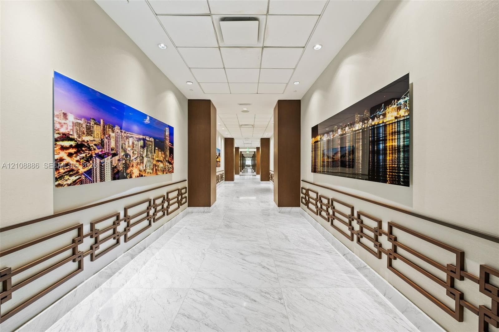 Corridor featuring stone-finish flooring, decorative geometric wall molding, recessed ceiling lighting, and structural columns with wood-finish paneling