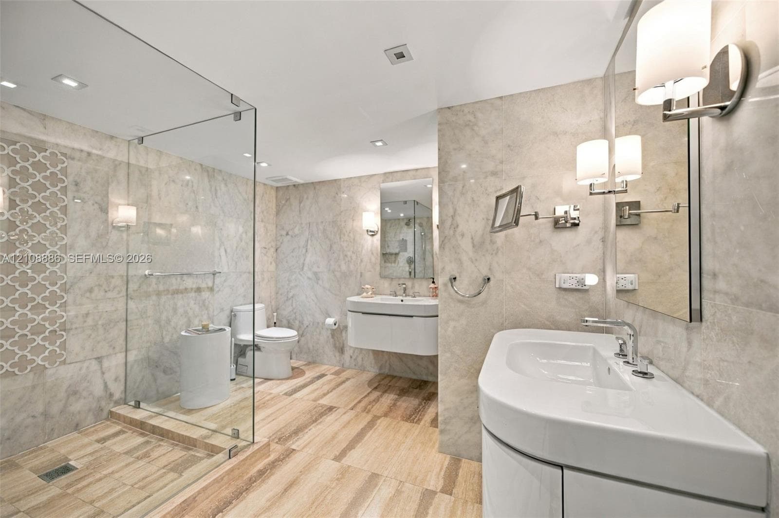 Bathroom featuring a frameless glass-enclosed shower with stone tiling, floating vanity with an integrated basin, stone wall cladding, and recessed lighting