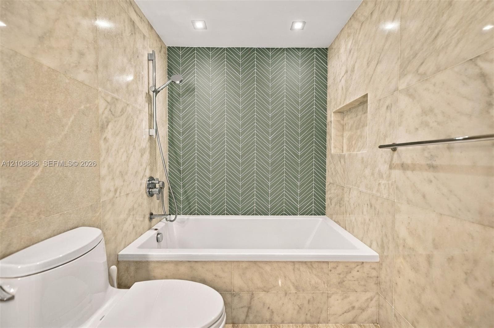 Bathroom featuring large-format stone wall tiling, a green herringbone-patterned tile accent wall, built-in recessed wall shelving, a deep soaking tub, and an adjustable-height hand-held shower fixture