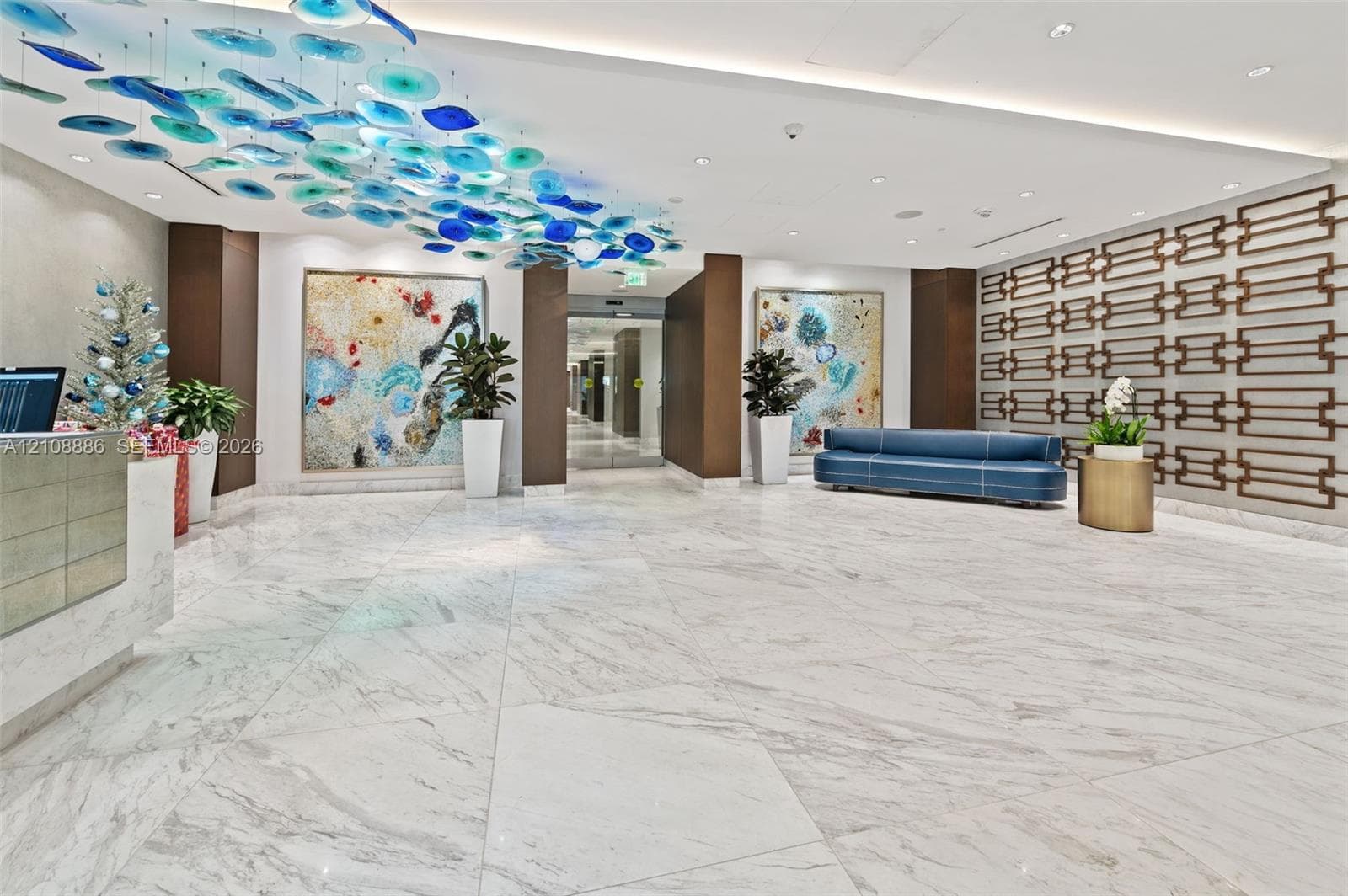 Expansive lobby featuring polished stone flooring, custom blue glass ceiling art, intricate bronze-tone geometric wall paneling, and recessed lighting
