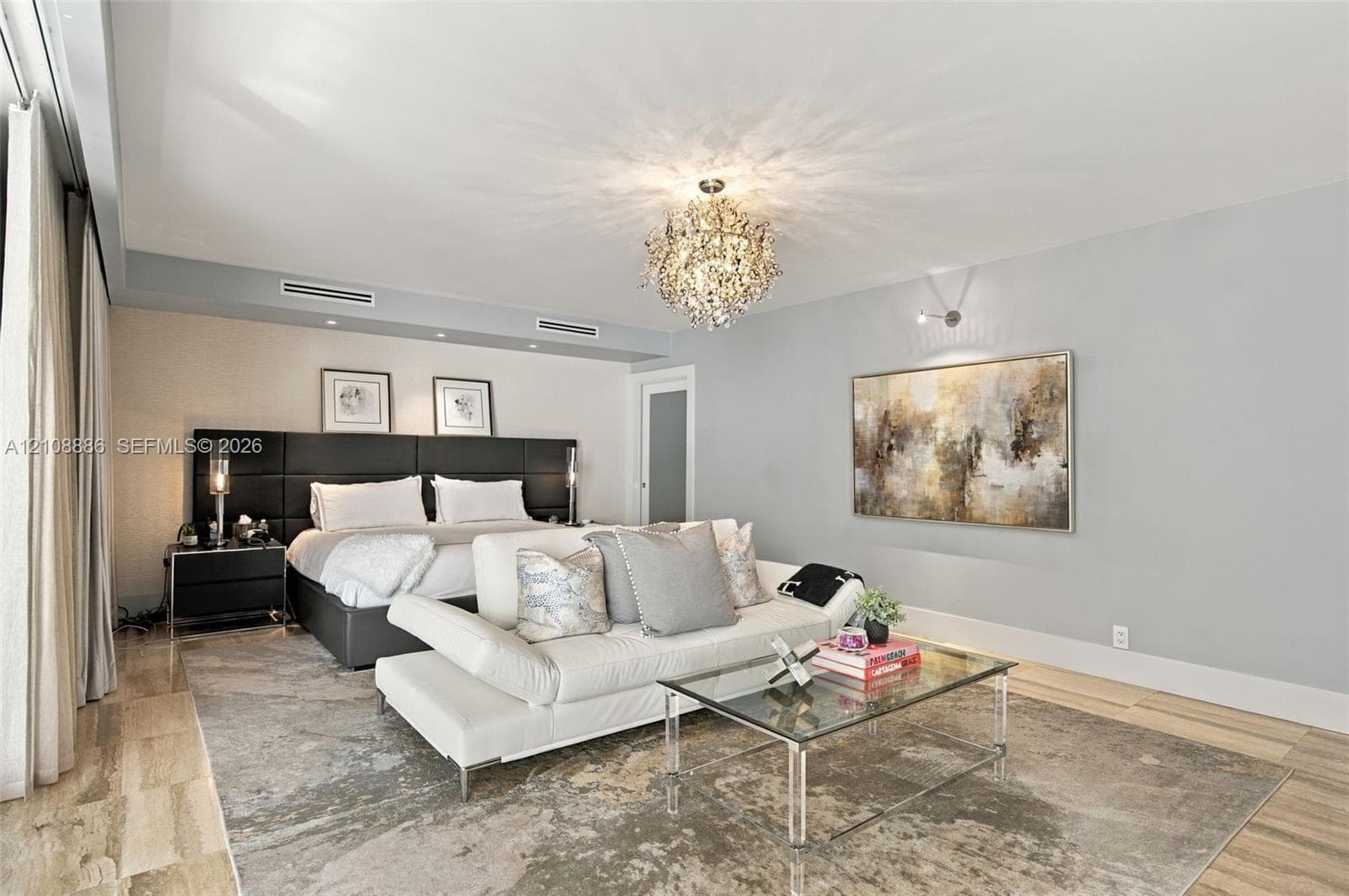 Spacious interior featuring stone flooring, a built-in upholstered headboard, a multifaceted crystal chandelier, and recessed ceiling lighting
