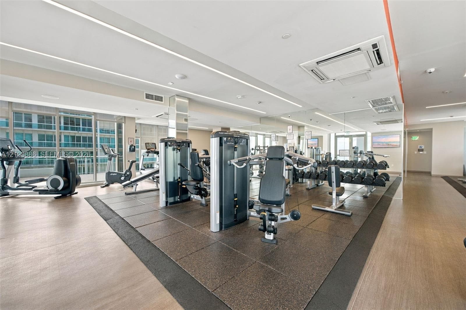 Fitness center featuring floor-to-ceiling windows, recessed linear lighting, rubberized gym flooring, and mirrored walls