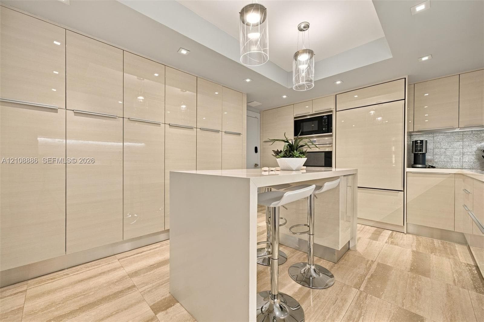 Kitchen featuring high-gloss cabinetry, stone-surface central island, built-in panel-ready appliances, recessed lighting with dual glass pendants, and stone tile flooring