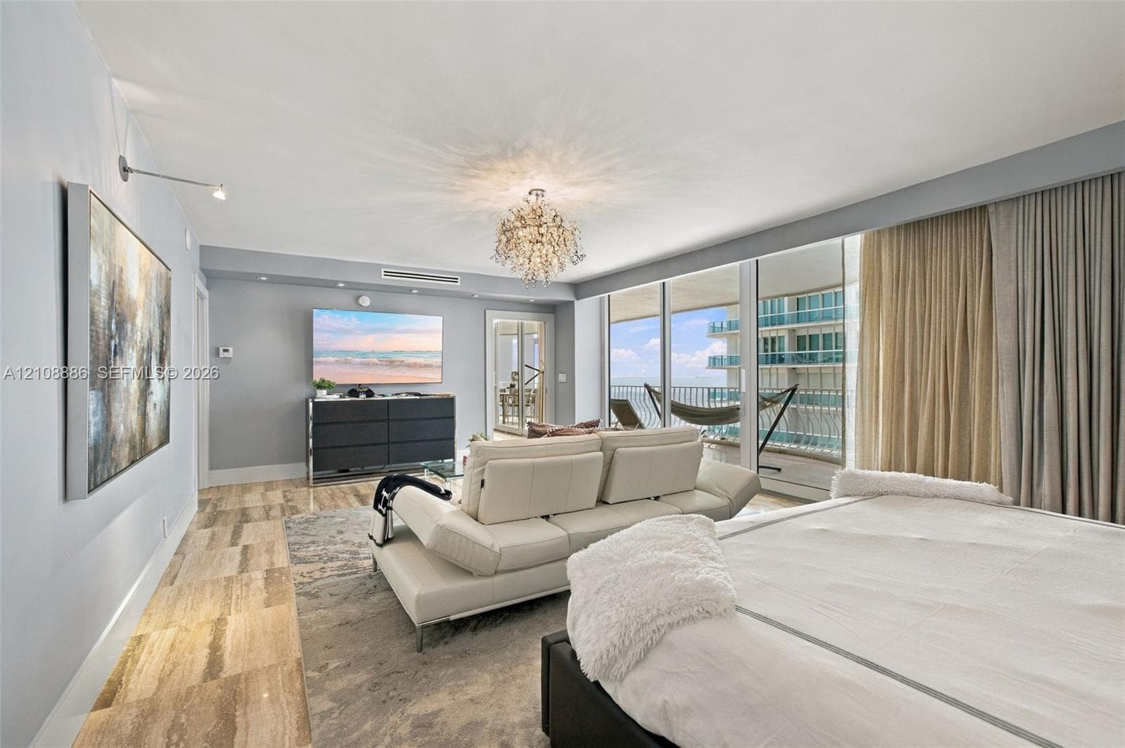 Expansive floor-to-ceiling glass sliding doors, stone tile flooring, built-in recessed ceiling lighting, ornate crystal chandelier, and integrated drapery pockets
