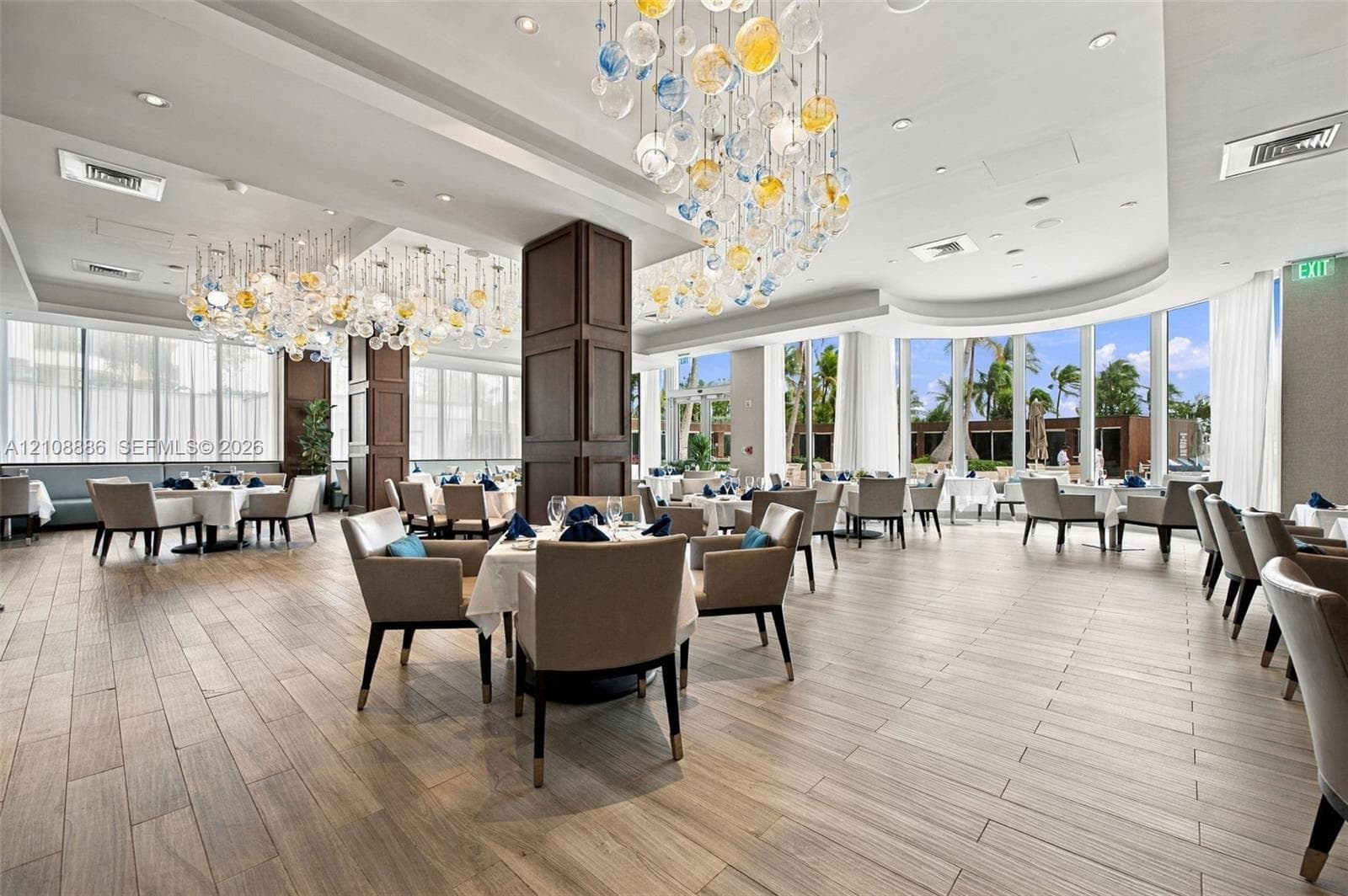 Open-concept space featuring floor-to-ceiling windows, wood-finish flooring, recessed lighting, decorative multi-colored glass pendant chandeliers, and dark wood-paneled columns