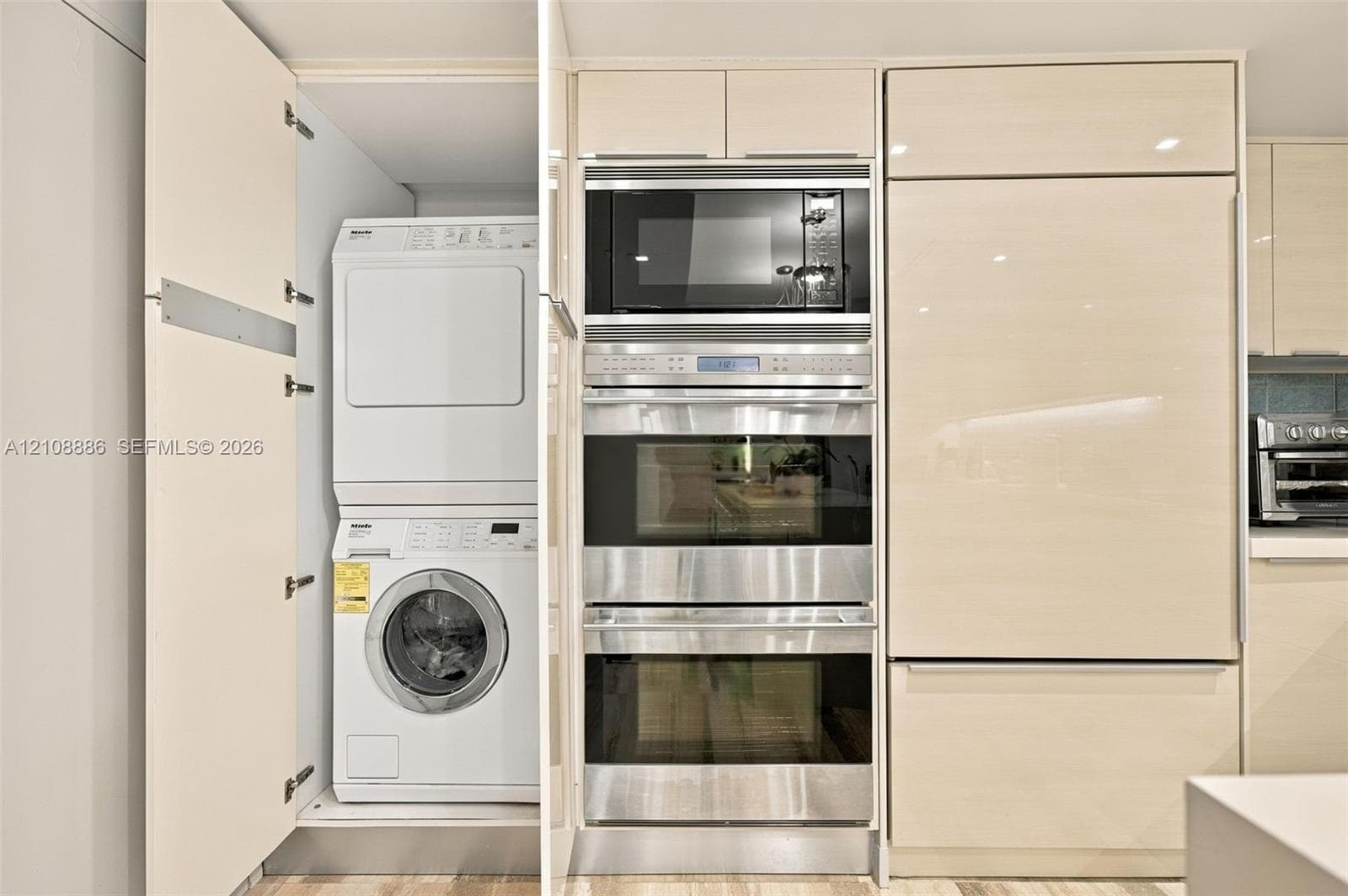 Built-in cabinetry featuring light wood-finish paneling, stackable laundry appliances, integrated stainless-steel wall oven, microwave, and paneled refrigerator