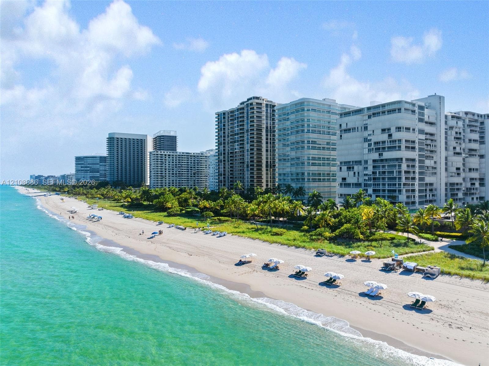 Coastal landscape featuring a wide sandy beach, turquoise shoreline, and lush palm vegetation