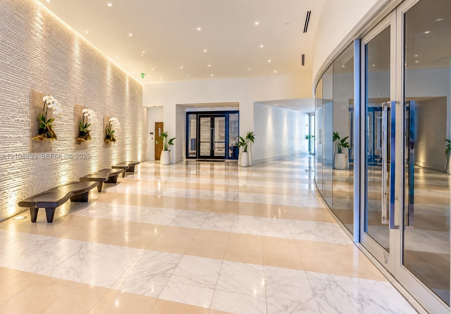 Grand lobby featuring a textured stone accent wall, large-format tile flooring, recessed ceiling lighting, and a curved floor-to-ceiling glass wall enclosure