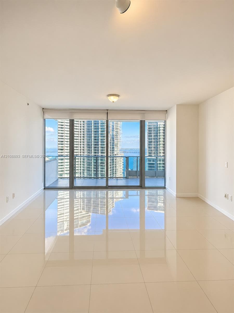 Floor-to-ceiling glass windows, ceramic tile flooring, and a glass-paneled balcony with panoramic water and skyline scenery