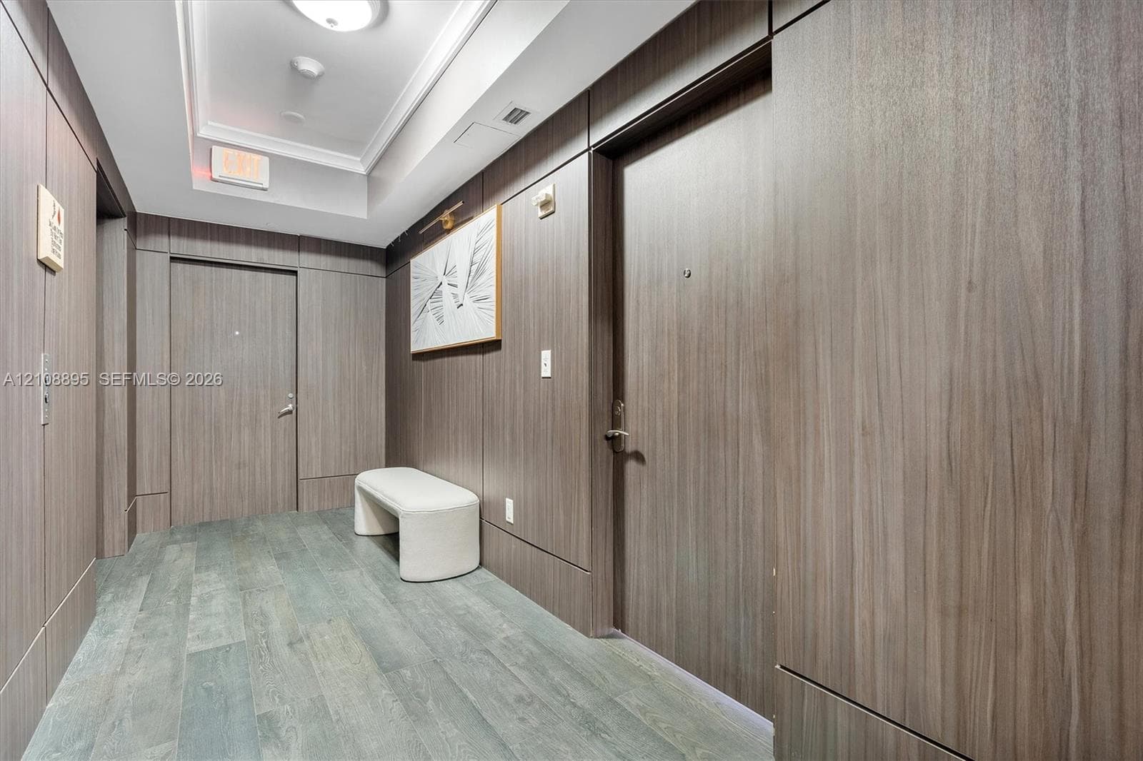 Hallway featuring wood-finish wall paneling, flush-mount lighting, tray ceiling, and wood-finish flooring