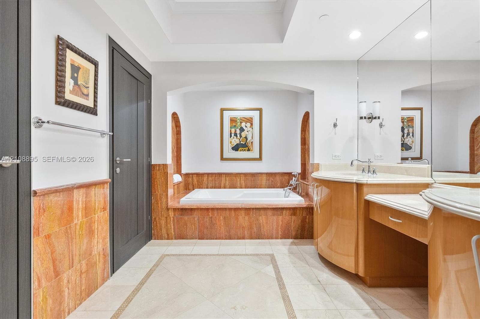 Bathroom featuring a built-in soaking tub surrounded by arched niches and stone wall cladding, a curved wooden vanity with a stone countertop, an expansive wall-to-wall mirror, and recessed ceiling lighting