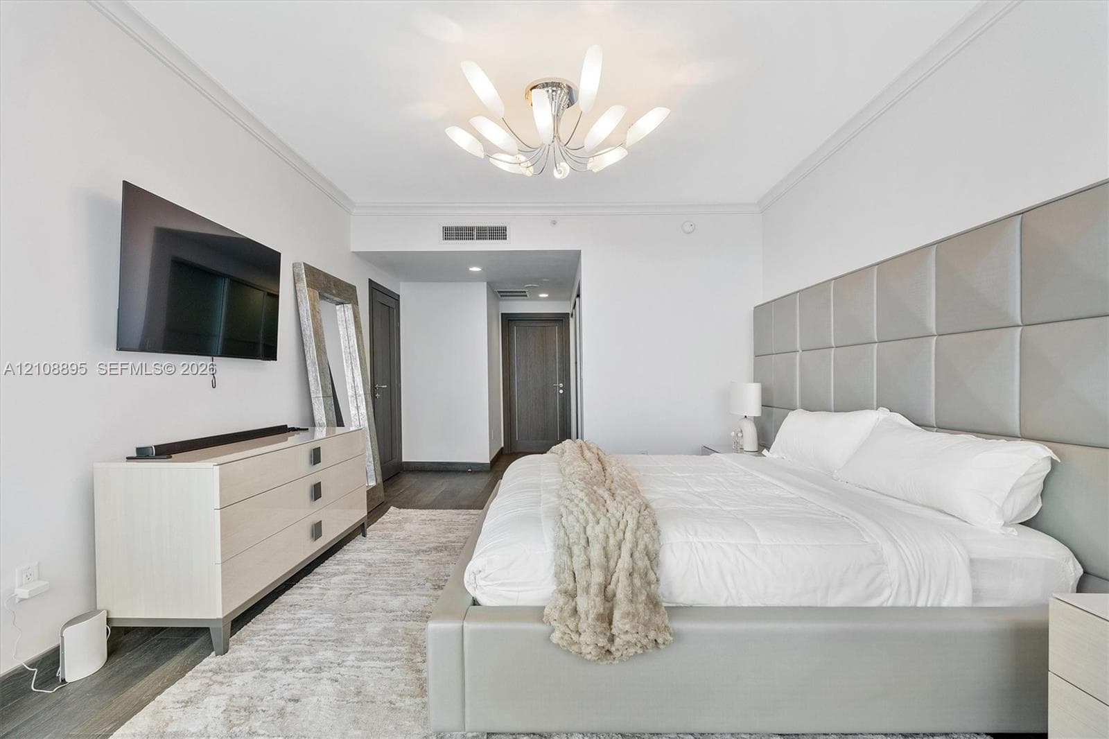Custom floor-to-ceiling tufted headboard, multi-arm sculptural light fixture, wood-finish flooring, and crown molding