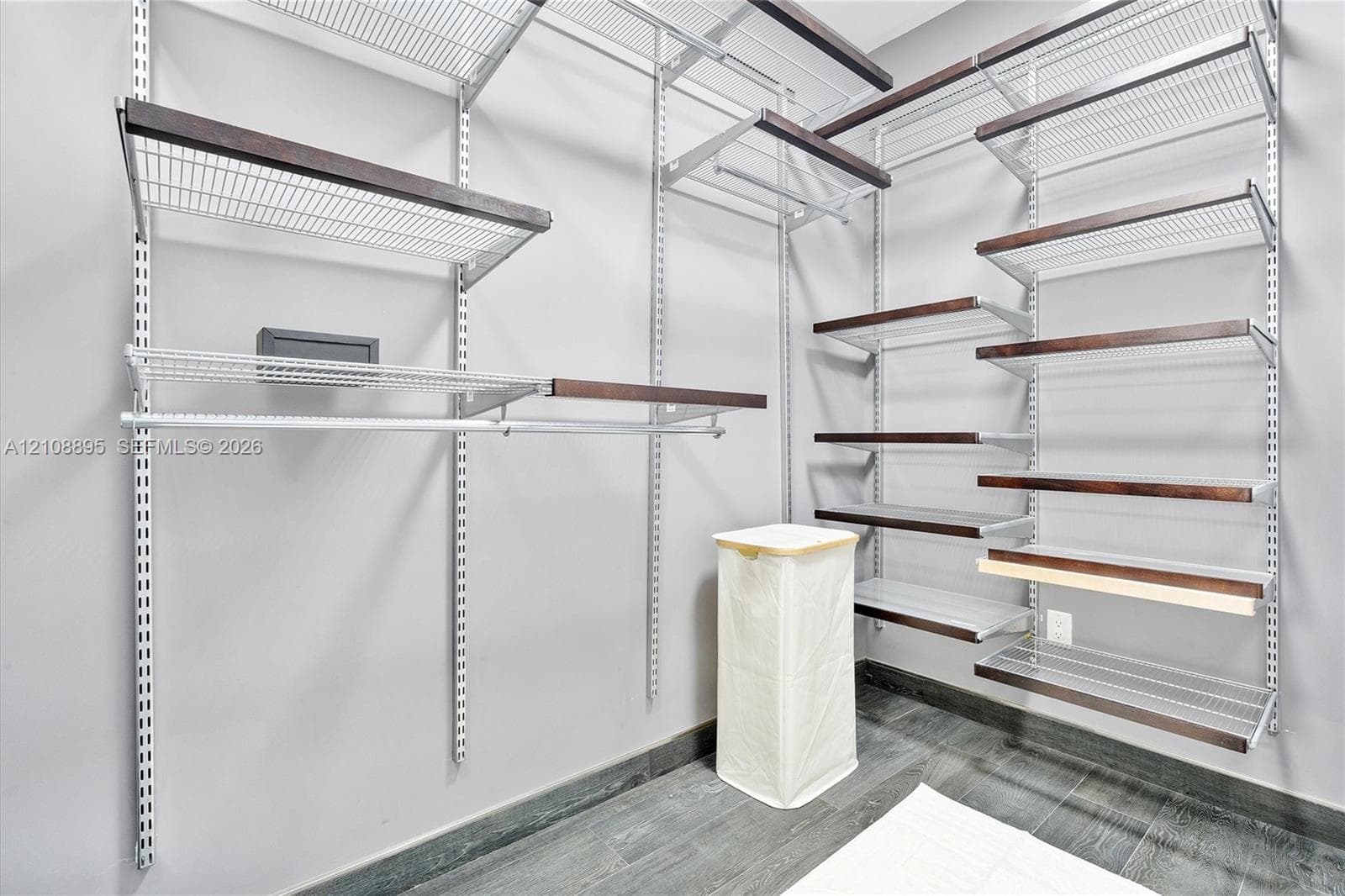 Customizable modular storage system featuring adjustable metal shelving with dark-toned wood trim and integrated hanging rods, complemented by dark wood-finish flooring