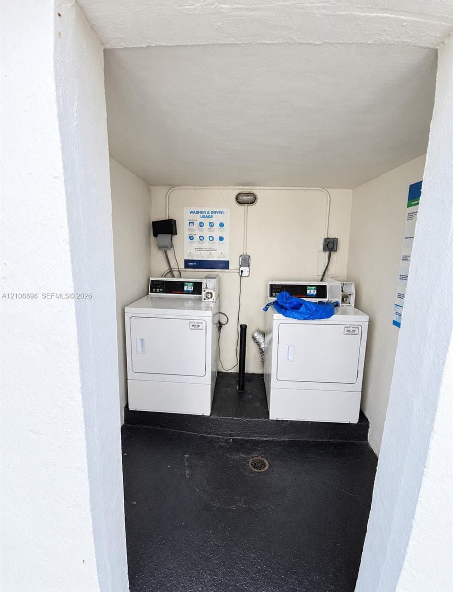 Dedicated laundry space featuring two white appliances, black flooring, and a floor drain