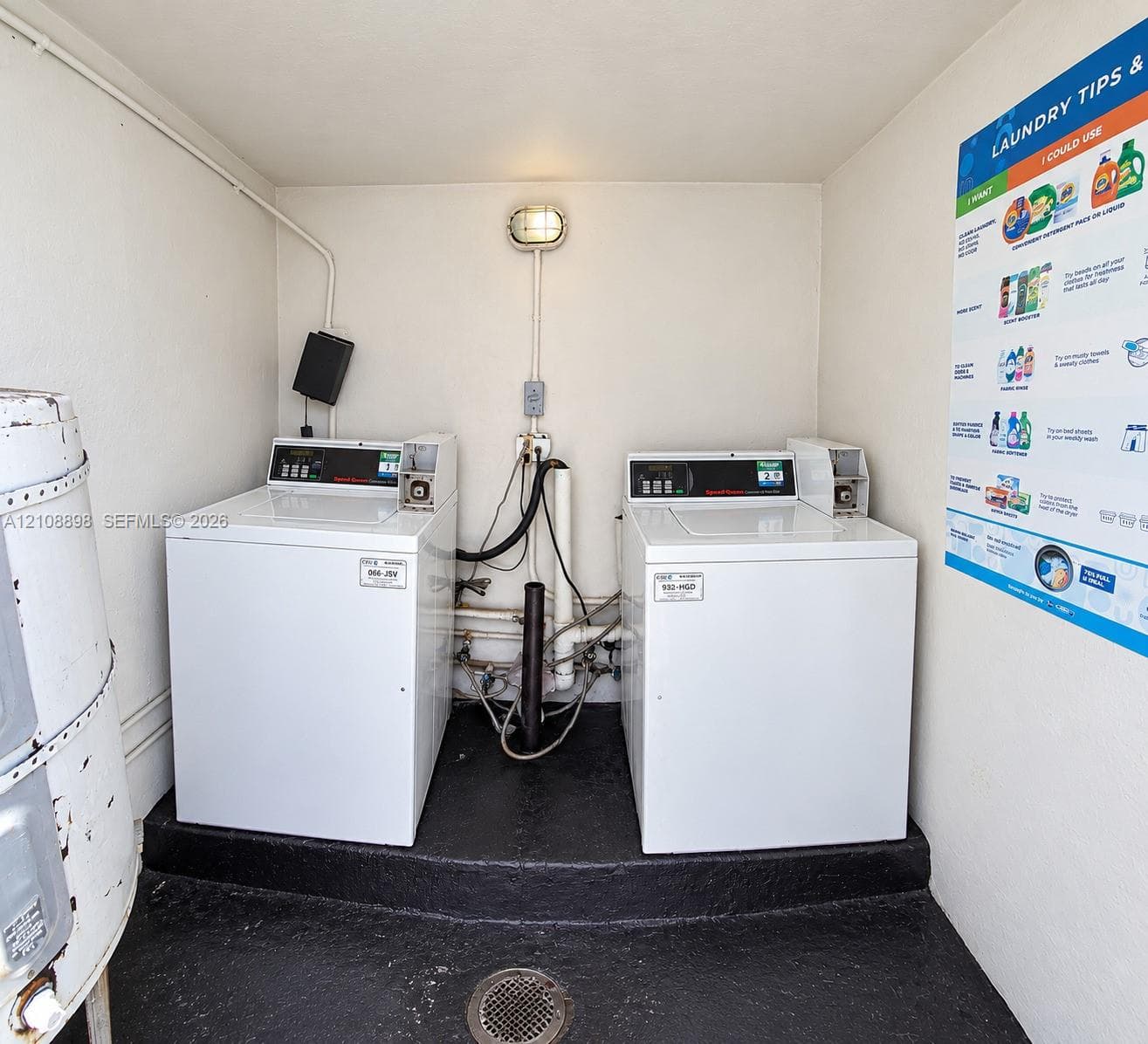 Laundry area featuring dual top-load washing machines, wall-mounted lighting, and a floor drain