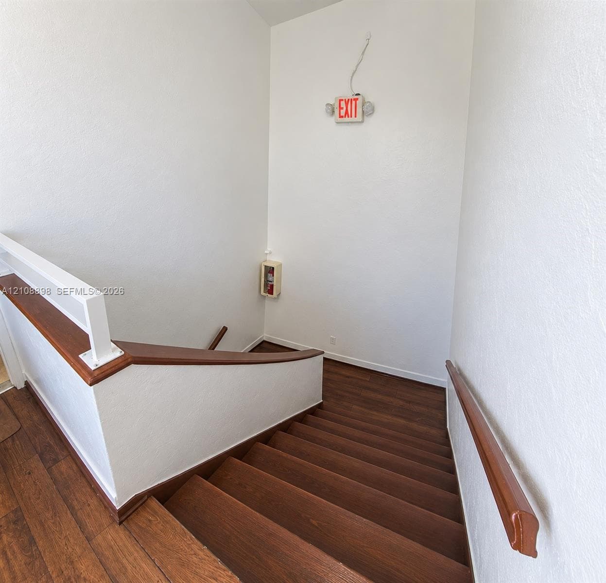 Staircase featuring wood-finish treads and landing, paired with a matching wood-finish wall-mounted handrail and a white-painted balustrade with a wood-finish cap