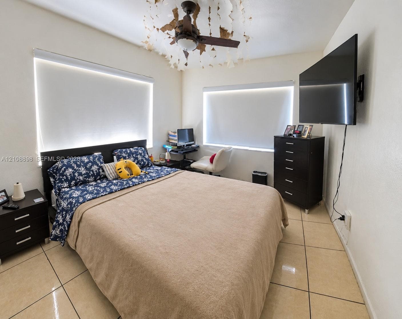 Tile flooring, multi-paneled ceiling fan with decorative light fixture, and two windows featuring motorized roller shades
