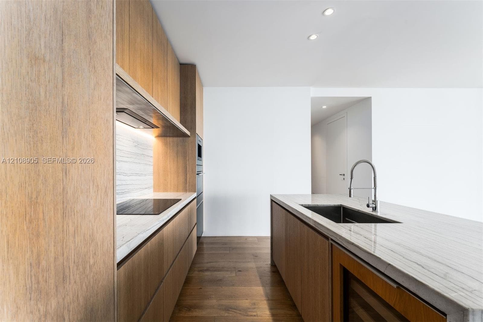 Kitchen featuring custom flat-panel wood-finish cabinetry, stone countertops, integrated cooktop, stainless steel faucet with undermount sink, and recessed ceiling lighting