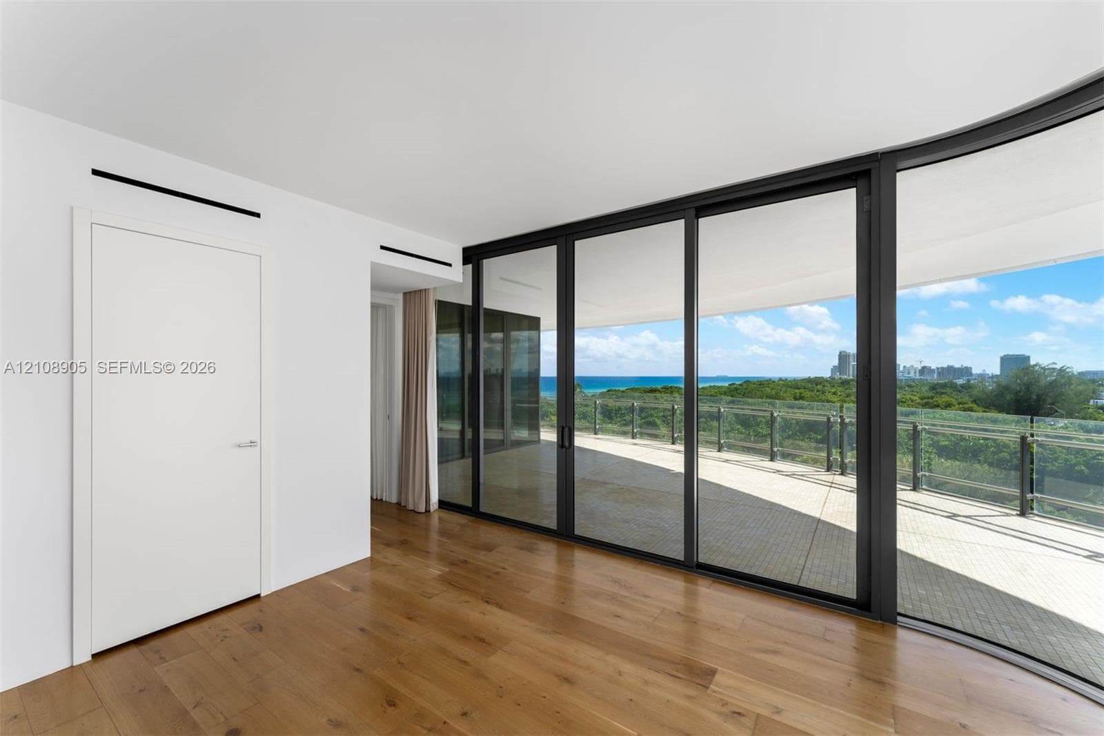 Floor-to-ceiling sliding glass doors, wood-finish flooring, and expansive covered balcony with glass railing